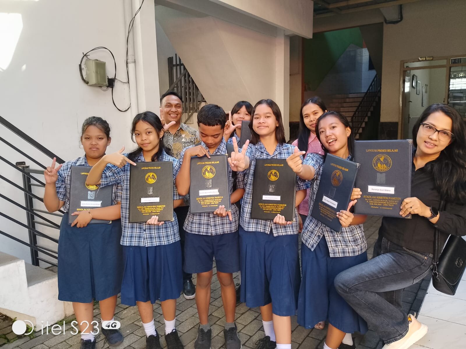 Leerlingen in schooluniform met een certificaat op de trap