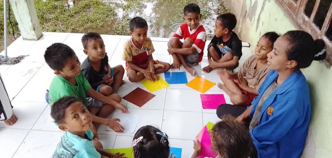 Een student geeft buiten les aan een groepje kinderen met gekleurde kaarten